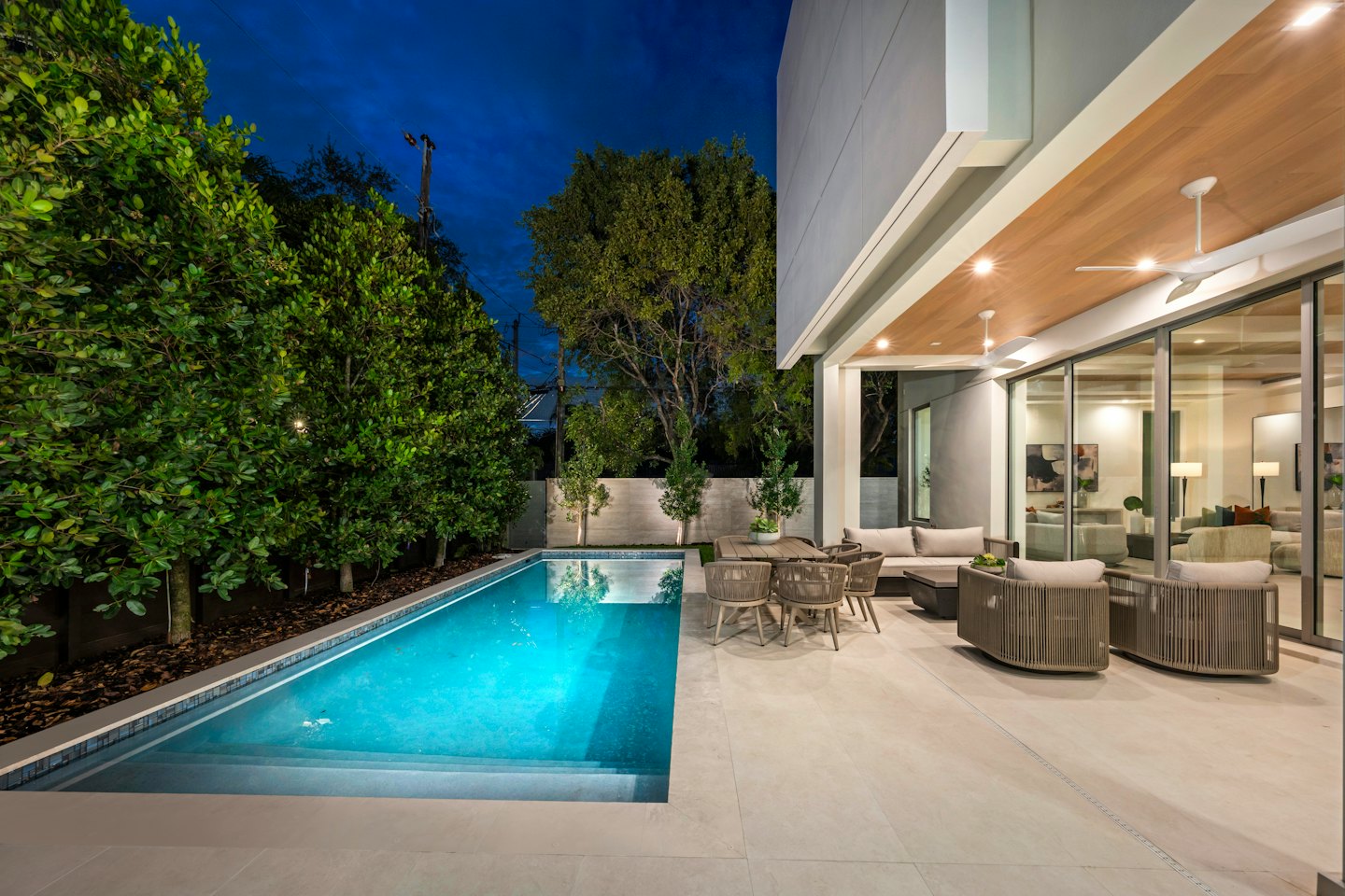 Moderne Luxus-Hausfassade mit beleuchtetem Pool und Terrasse in der Dämmerung.